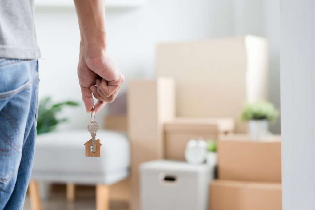 Moving Story Moving Home Alone Moving house, relocation. Man hold key house keychain in new apartment, inside the room was a cardboard box containing personal belongings and furniture. move in the apartment or condominium
