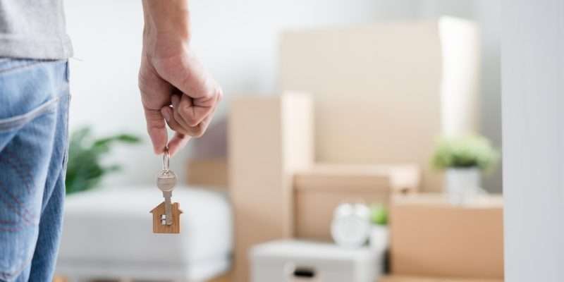 Moving Story Moving Home Alone Moving house, relocation. Man hold key house keychain in new apartment, inside the room was a cardboard box containing personal belongings and furniture. move in the apartment or condominium